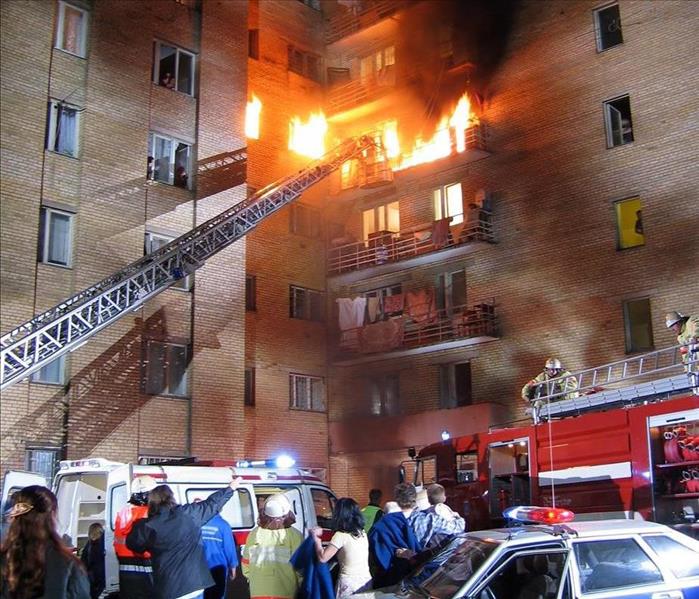 Image of an apartment complex on fire and fire fighters working to put out the fire.