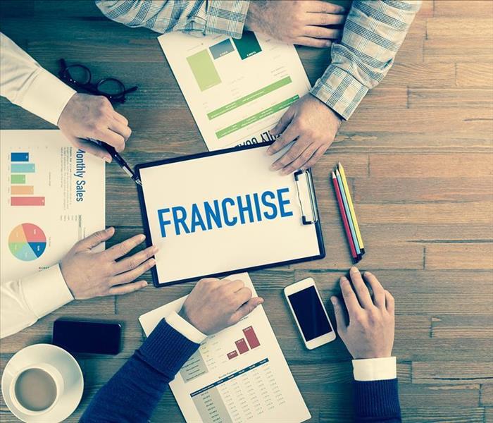 Image of a group of workers meeting on a table with a paper in the middle stating "Franchise" 